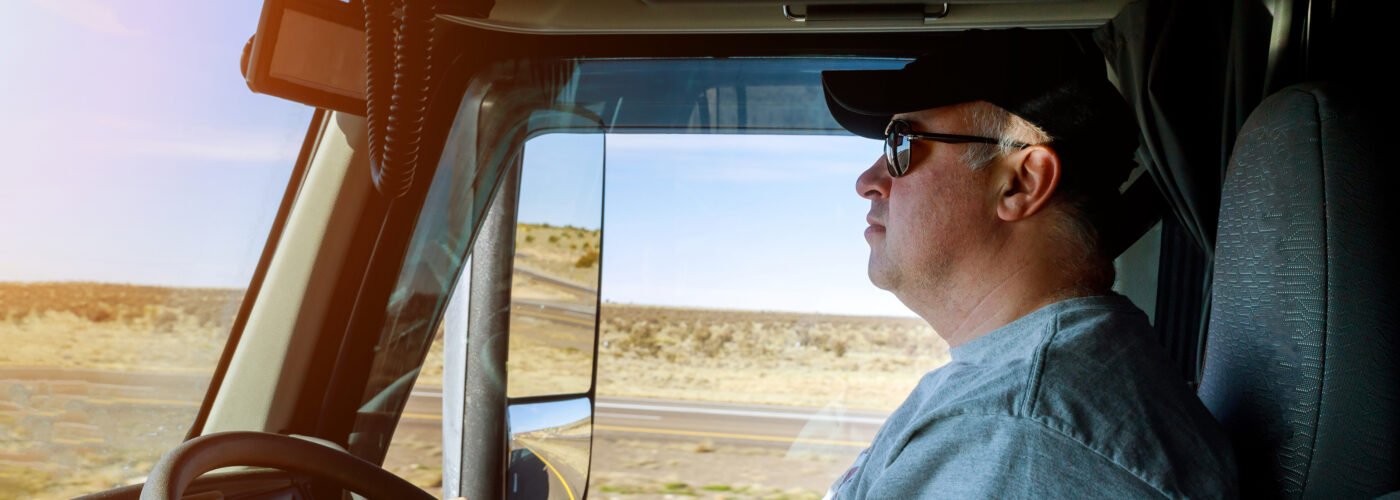 Owner operator truck driver standing near truck on highway showing stress and loss of control in no forced dispatch situation